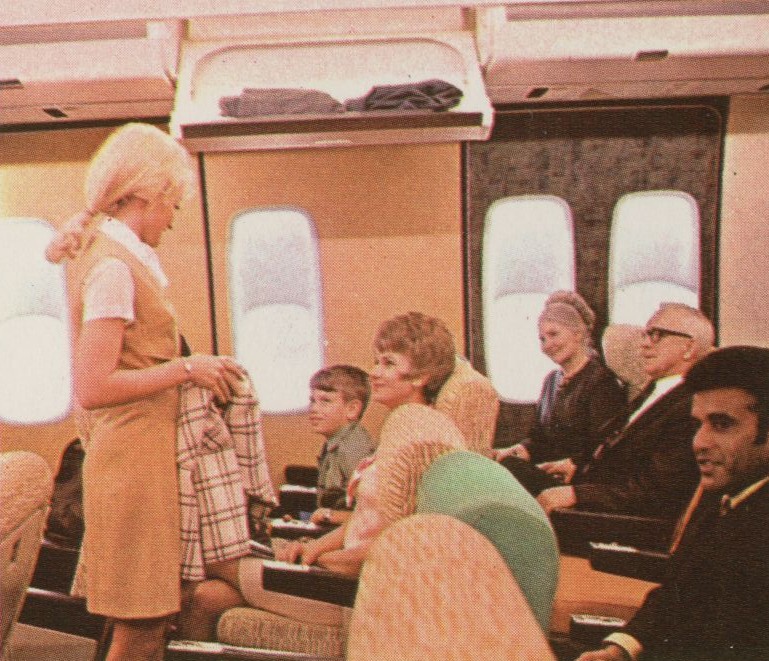 1970 A Flight Attendant in the Galaxy Gold uniform speaks with customers in the economy cabin of a mock up 747.
